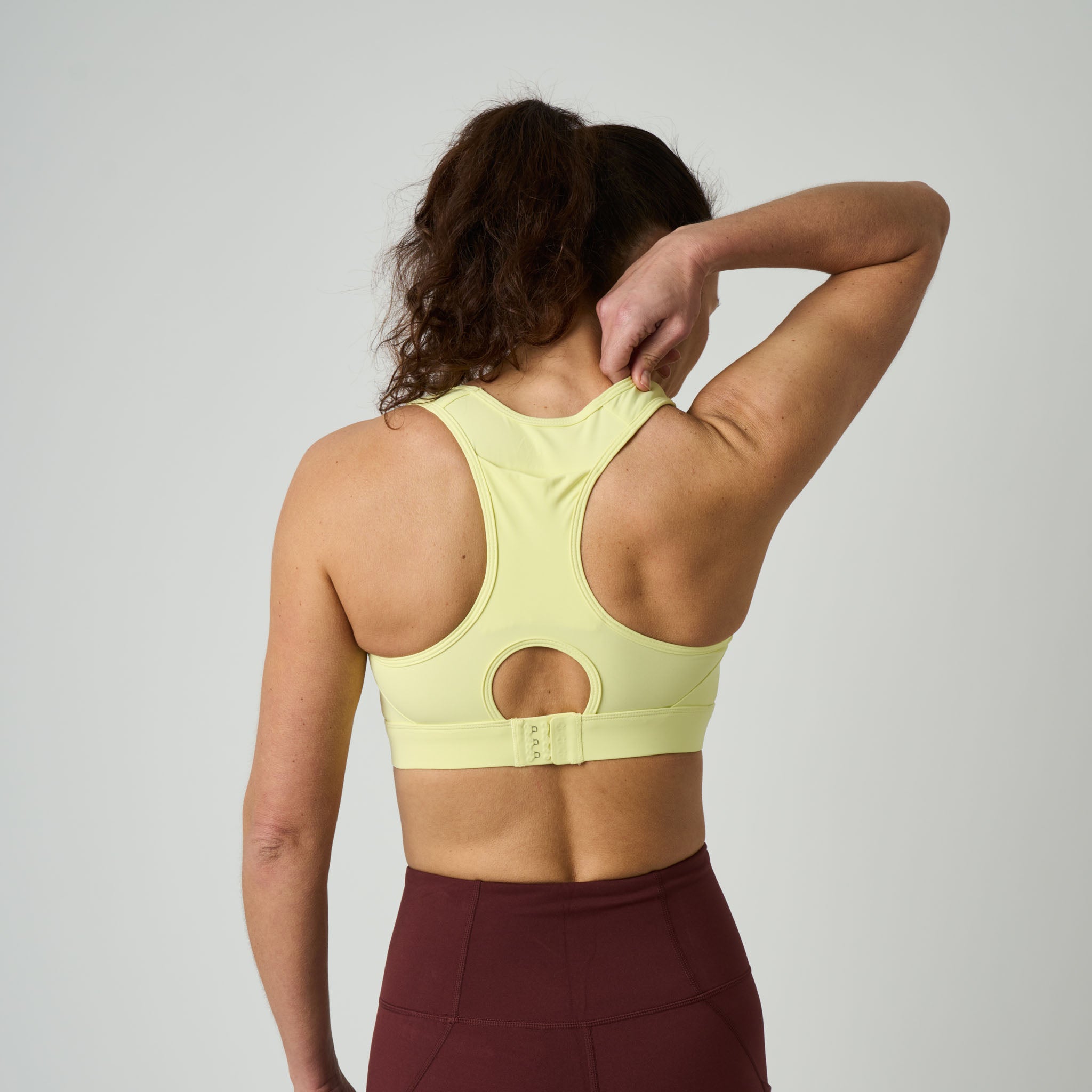 Person wearing a light yellow sports bra and maroon leggings on a plain background