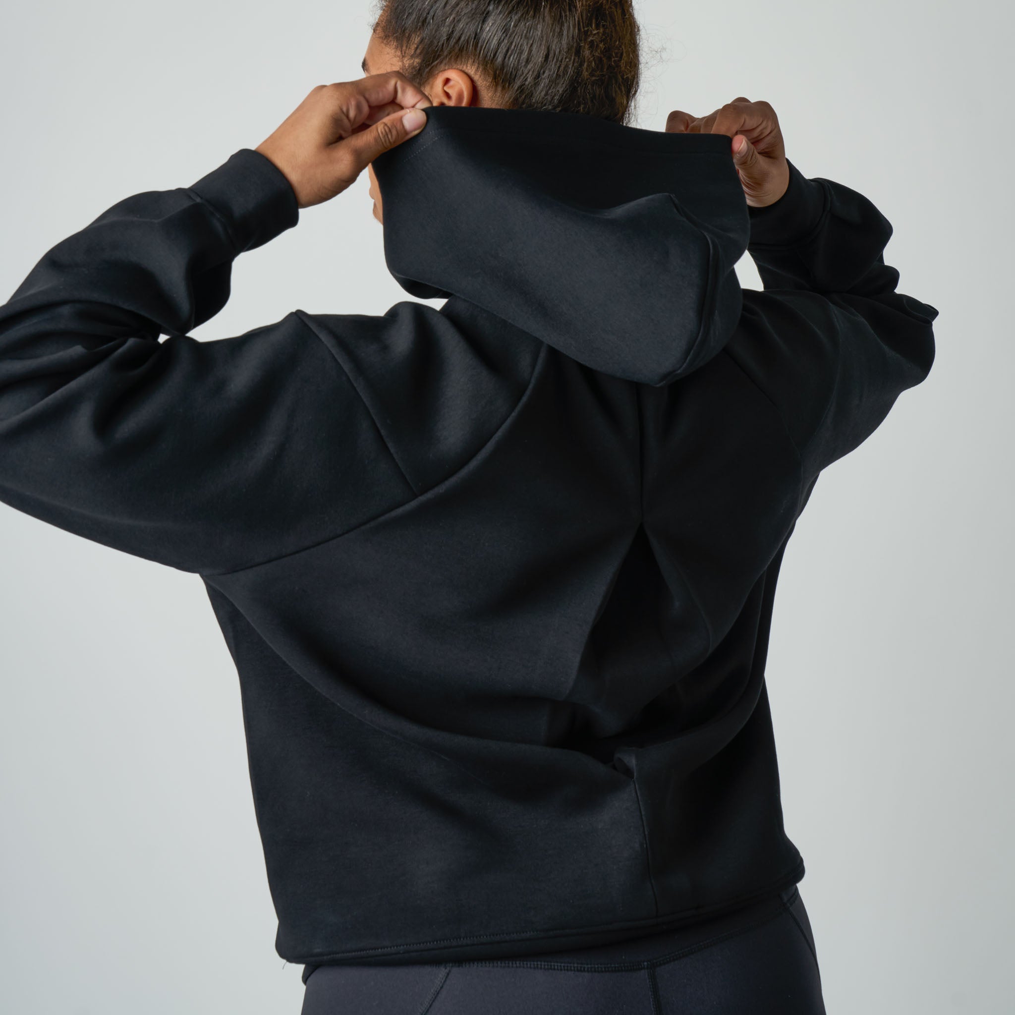 Person wearing a black hoodie with the back to the camera on a light gray background