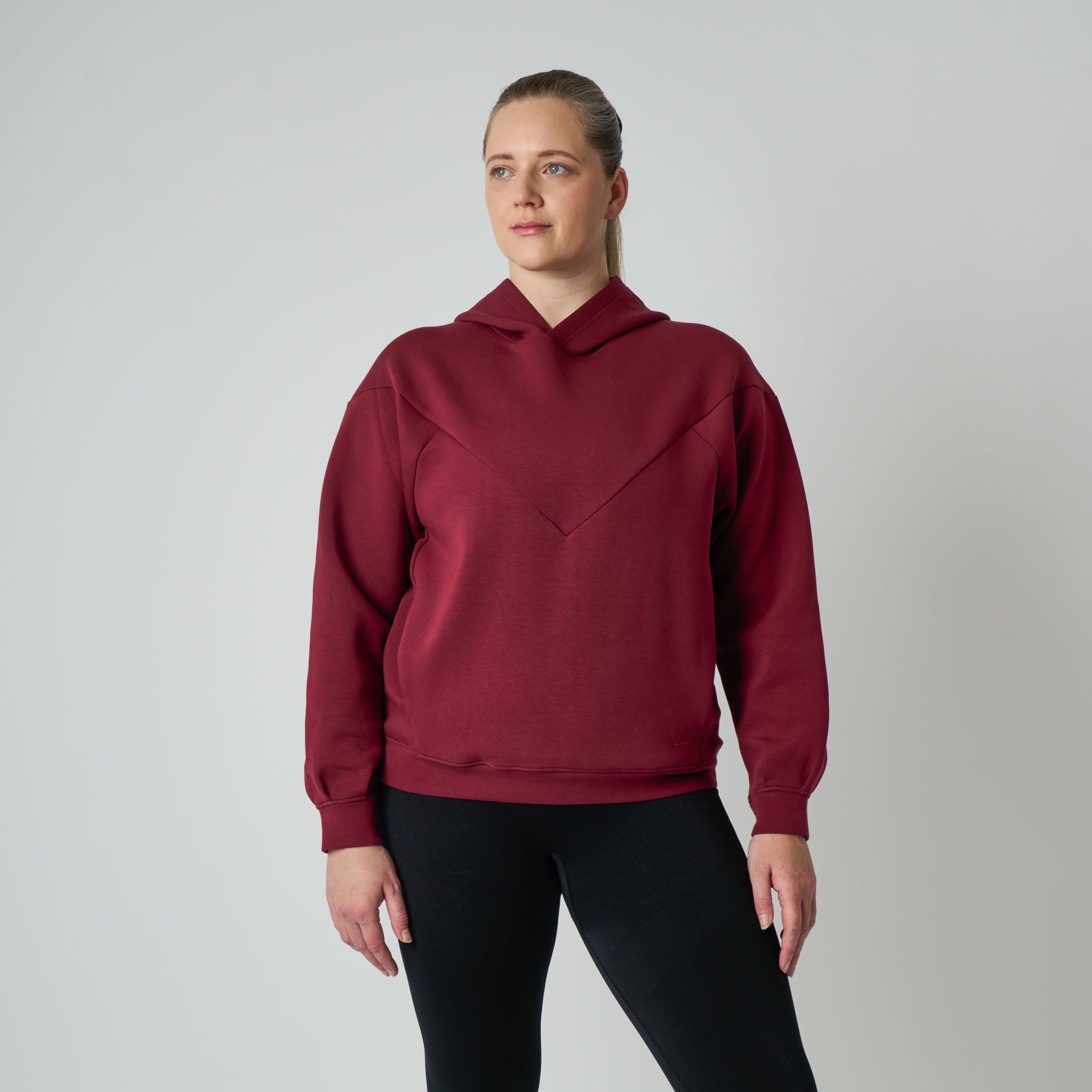 Person wearing a maroon hoodie and black pants on a gray background