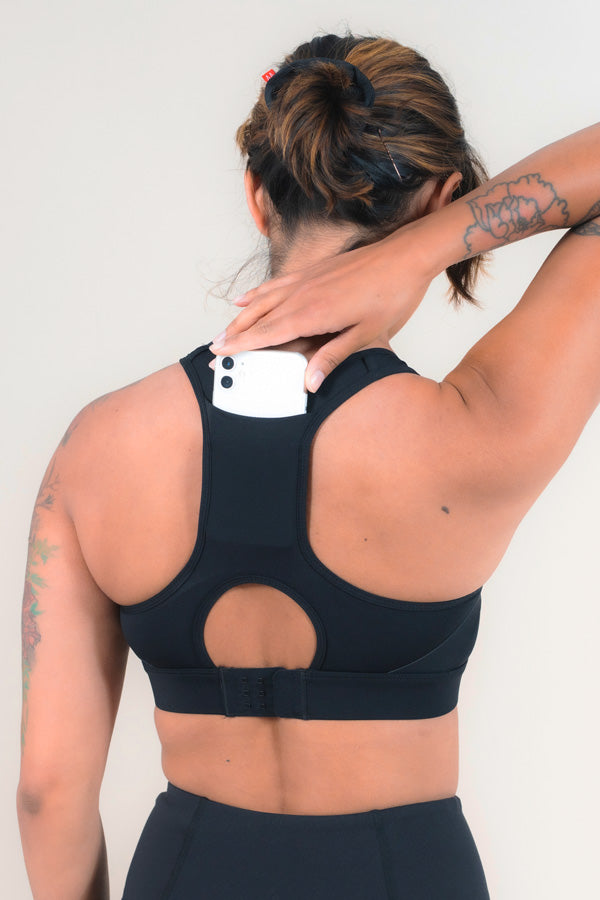 Woman placing an iPhone into the back pocket of the MAAREE Empower Sports Bra