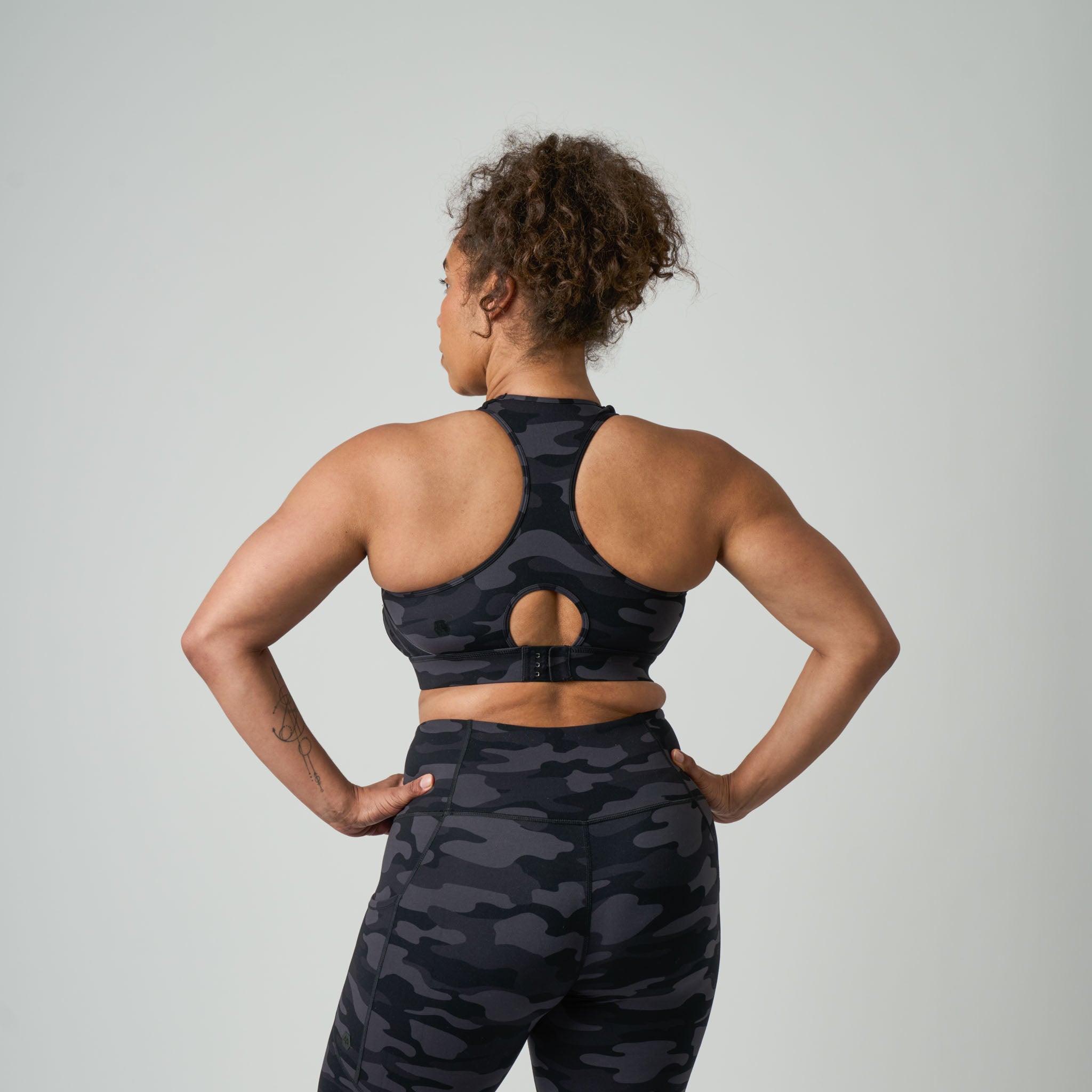 Person wearing a black camouflage sports bra and leggings on a light gray background