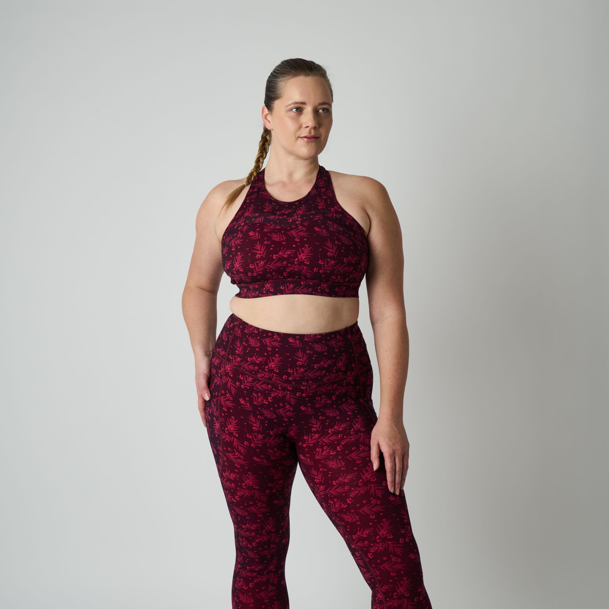 Woman wearing a maroon sports bra and leggings set on a gray background