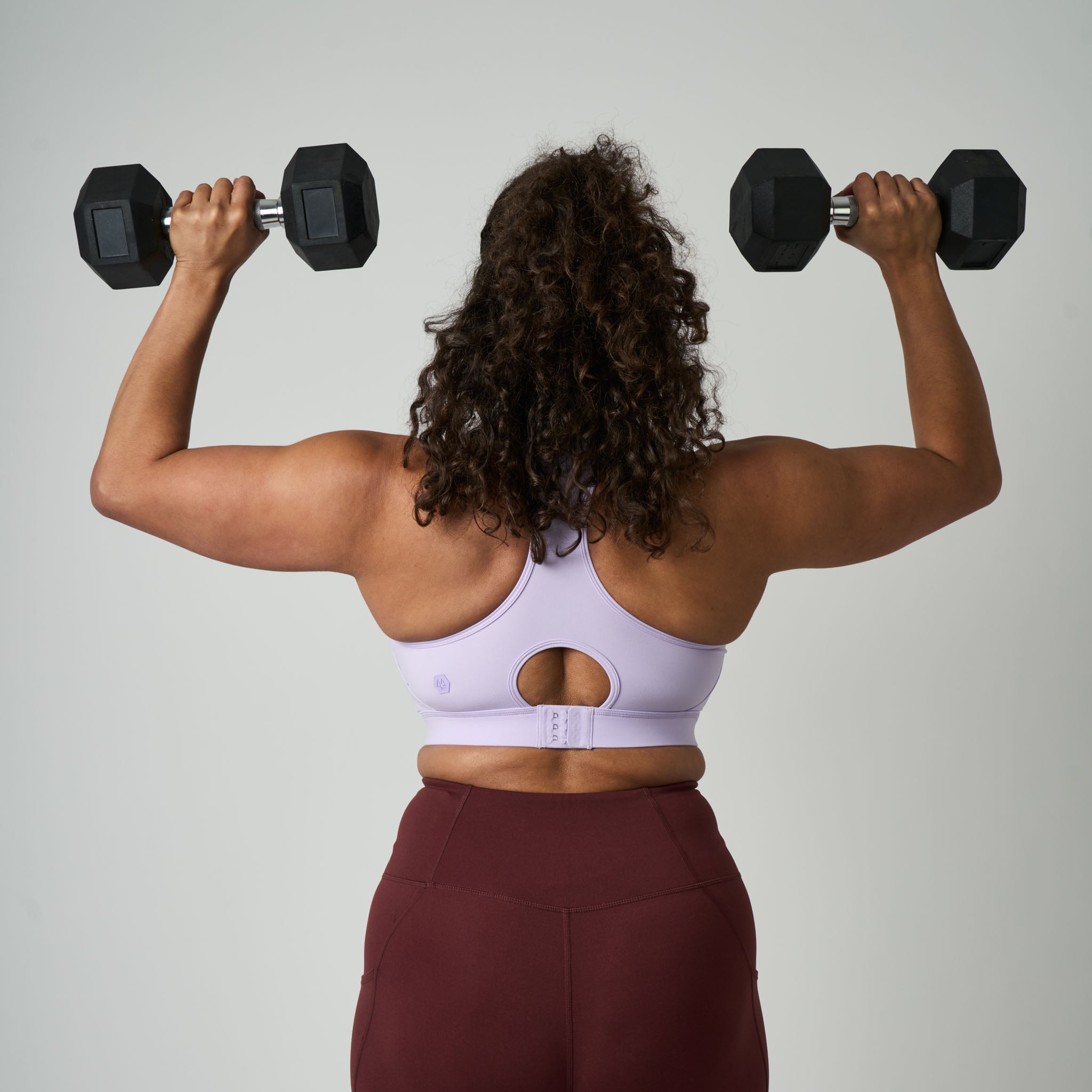 Person lifting dumbbells from behind on a plain background