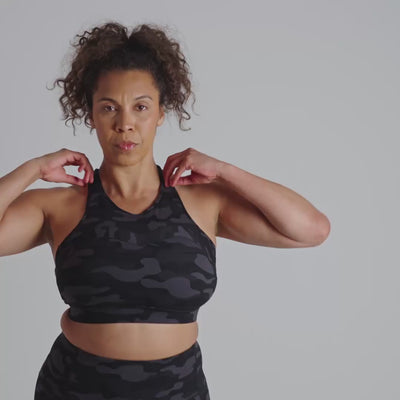 Woman wearing a black camouflage sports bra against a plain background